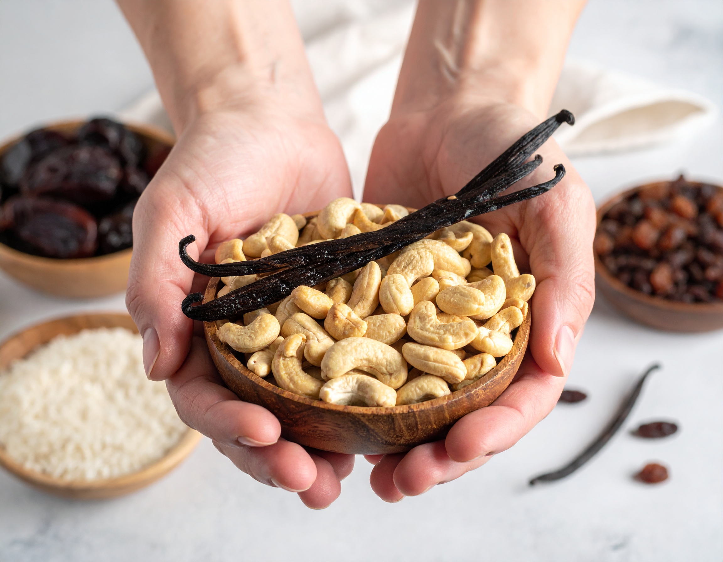 Holzschale mit Cashewkernen und Vanilleschoten, die von 2 Händen gehalten wird - KI-generiert