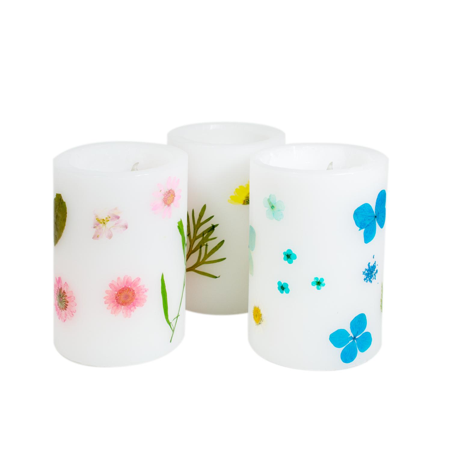 Drei runde weiße Windlichter mit verschiedenfarbigen  Blüten