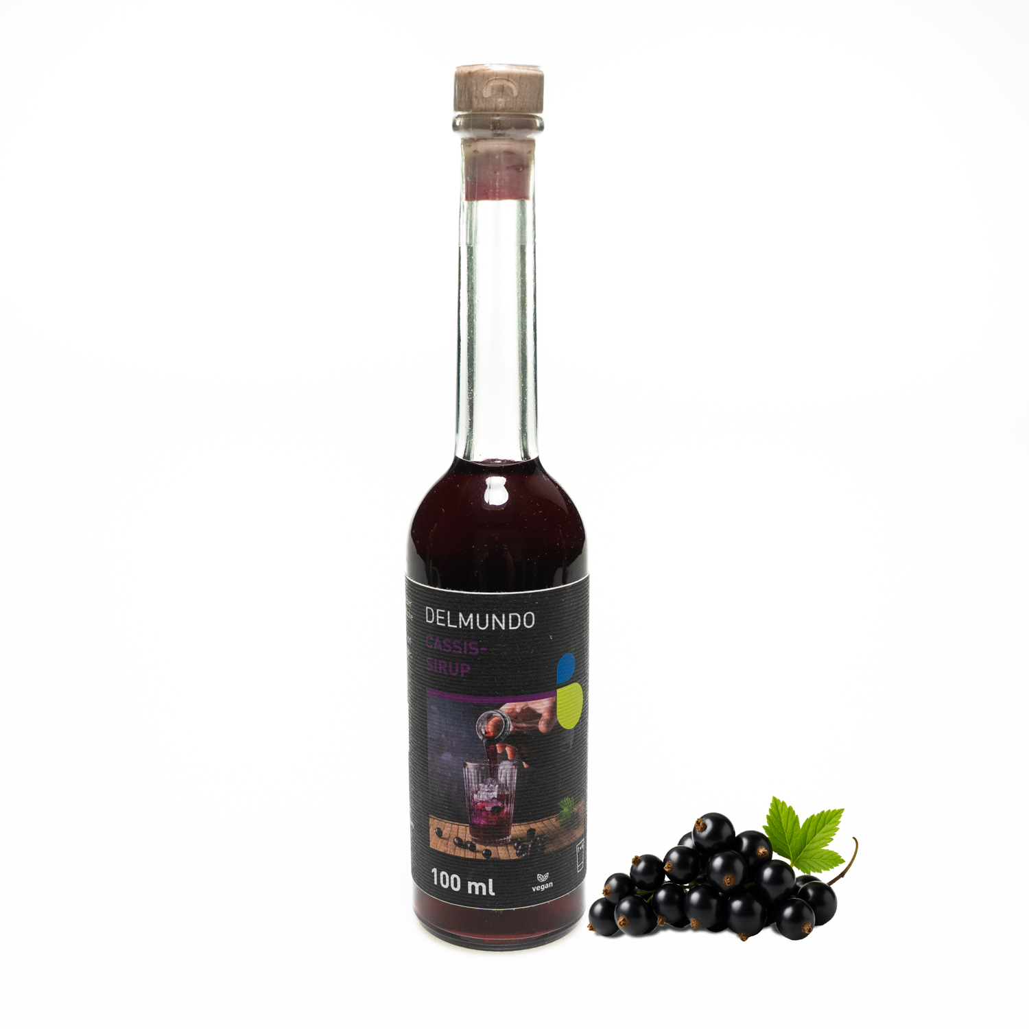 Eine klare Glasflasche mit Bügel-Verschluss gefüllt mit dunklem Cassis-Sirup. Daneben liegt ein Strauch Cassisbeeren.